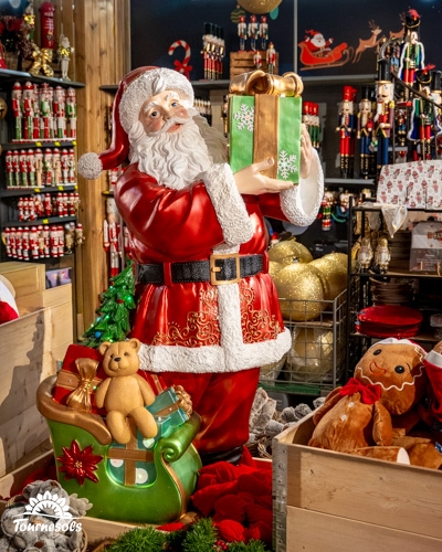 Statue de Père Noël tenant un cadeau dans un marché de Noël décoré.